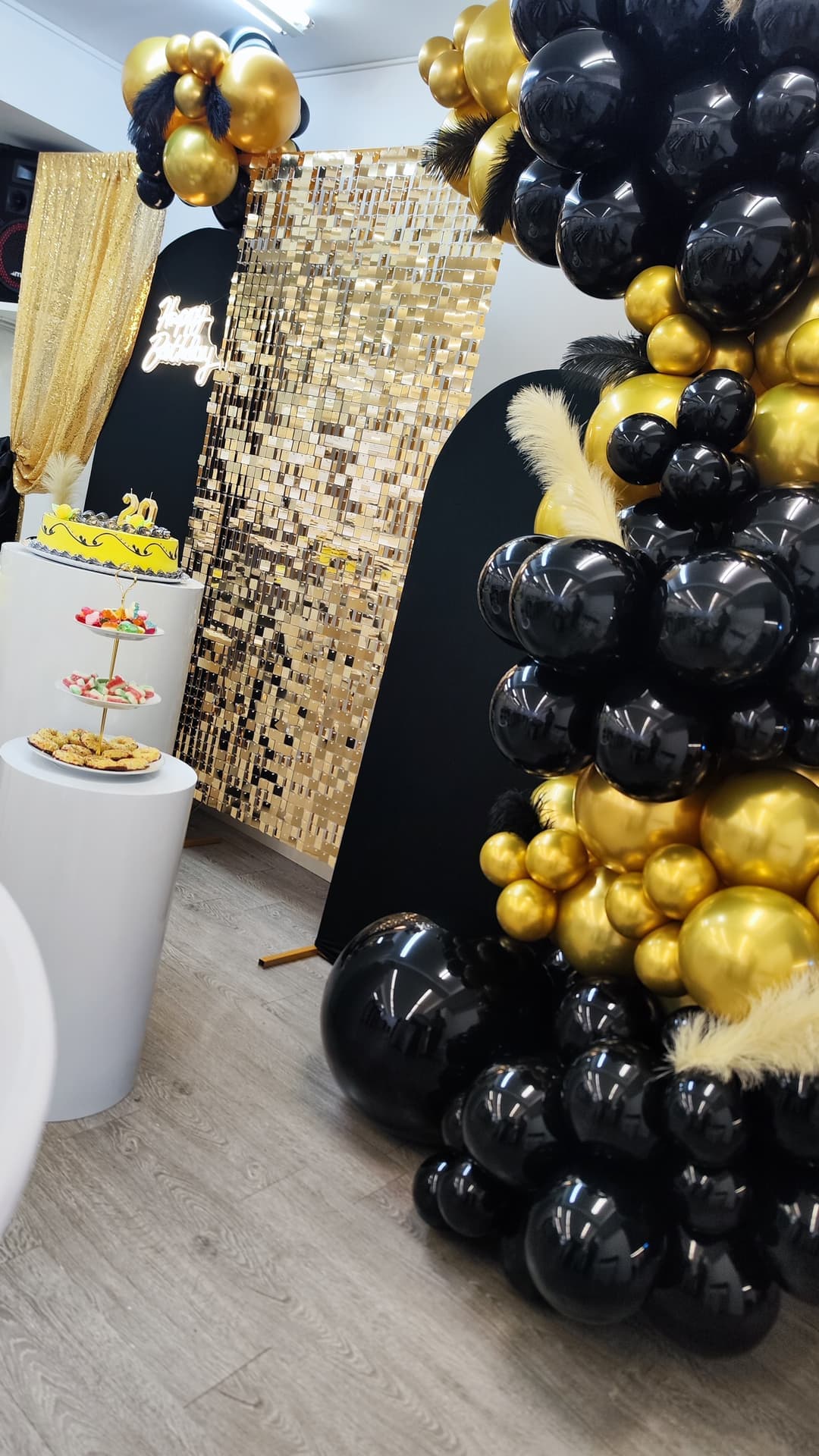 Fondo de lentejuelas doradas con arco de globos negros y dorados junto a la mesa de la tarta