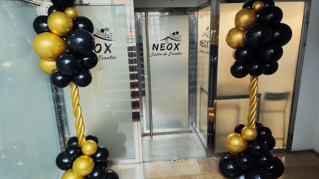 Entrada del salón NEOX decorada con dos columnas de globos negros y dorados